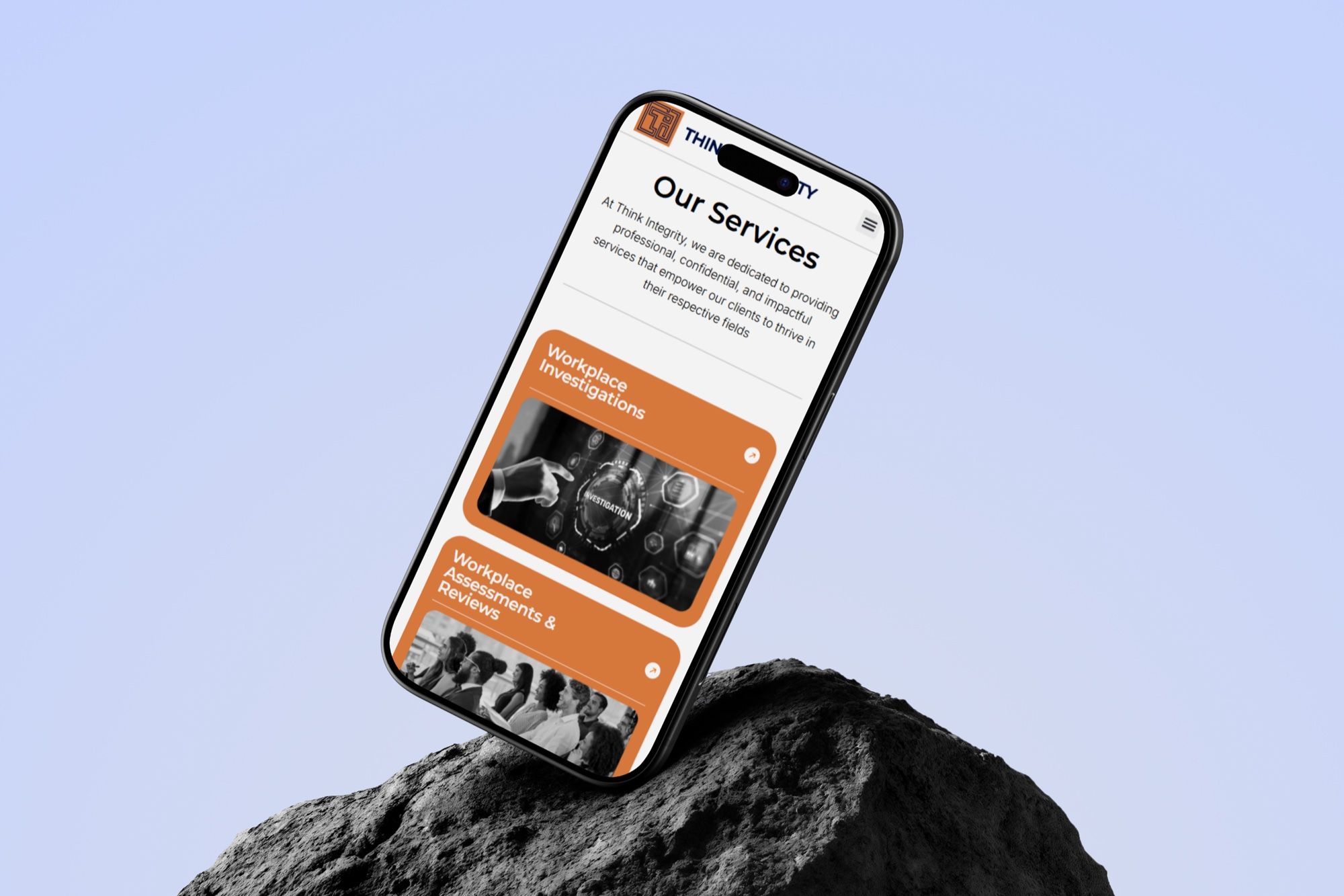A phone balanced on a dark rock against a lavender background, showing the Think Integrity services page with orange service cards.